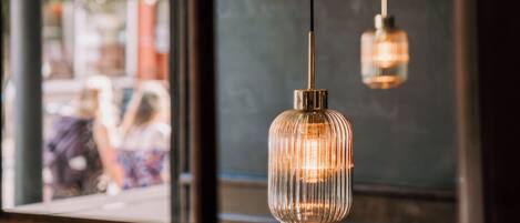 A restaurant interior with a chalkboard menu, hanging pendant lights, and a view through the window.