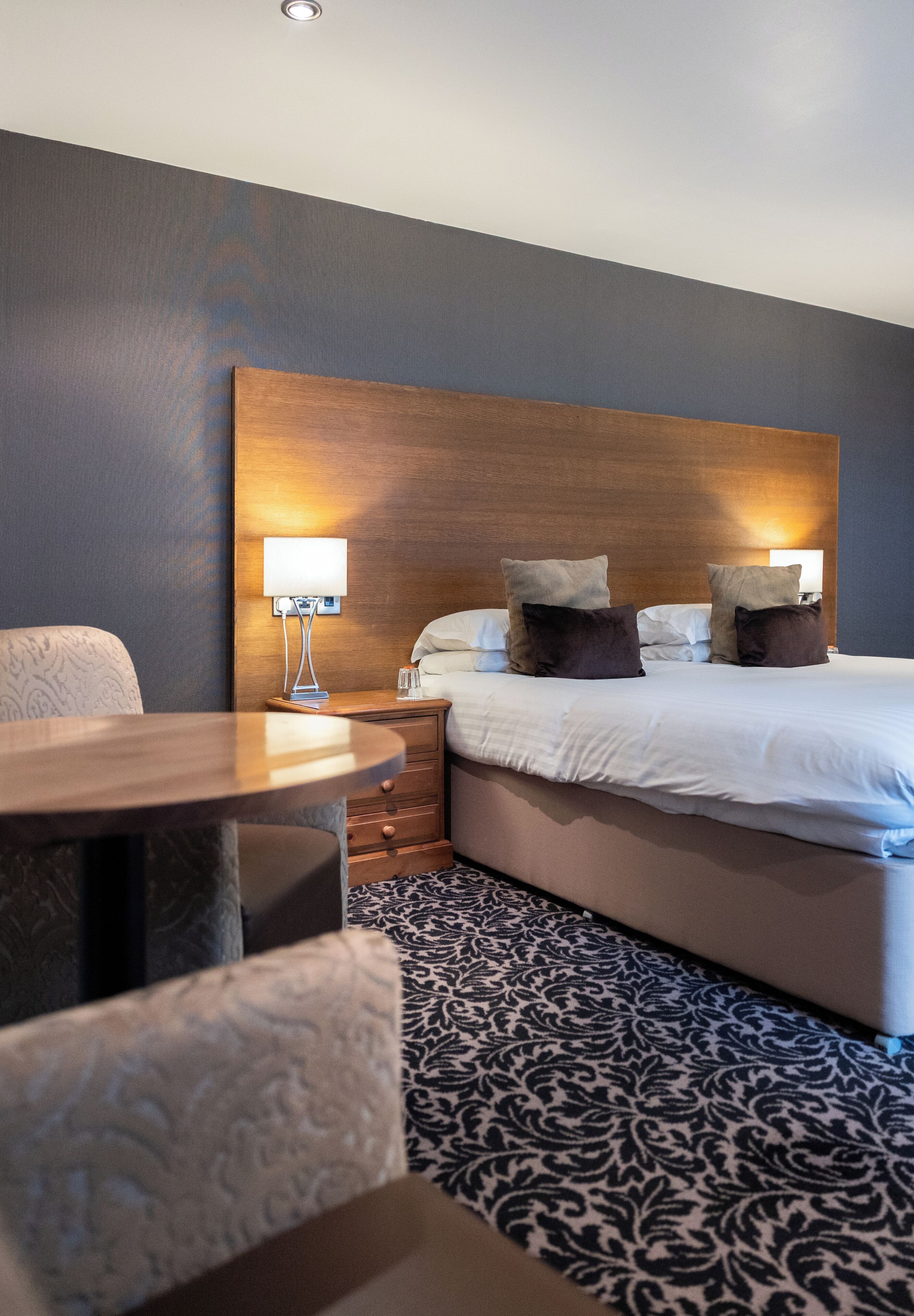 Une chambre d’hôtel avec un lit, des tables de chevet, une lampe et un tapis à motifs.