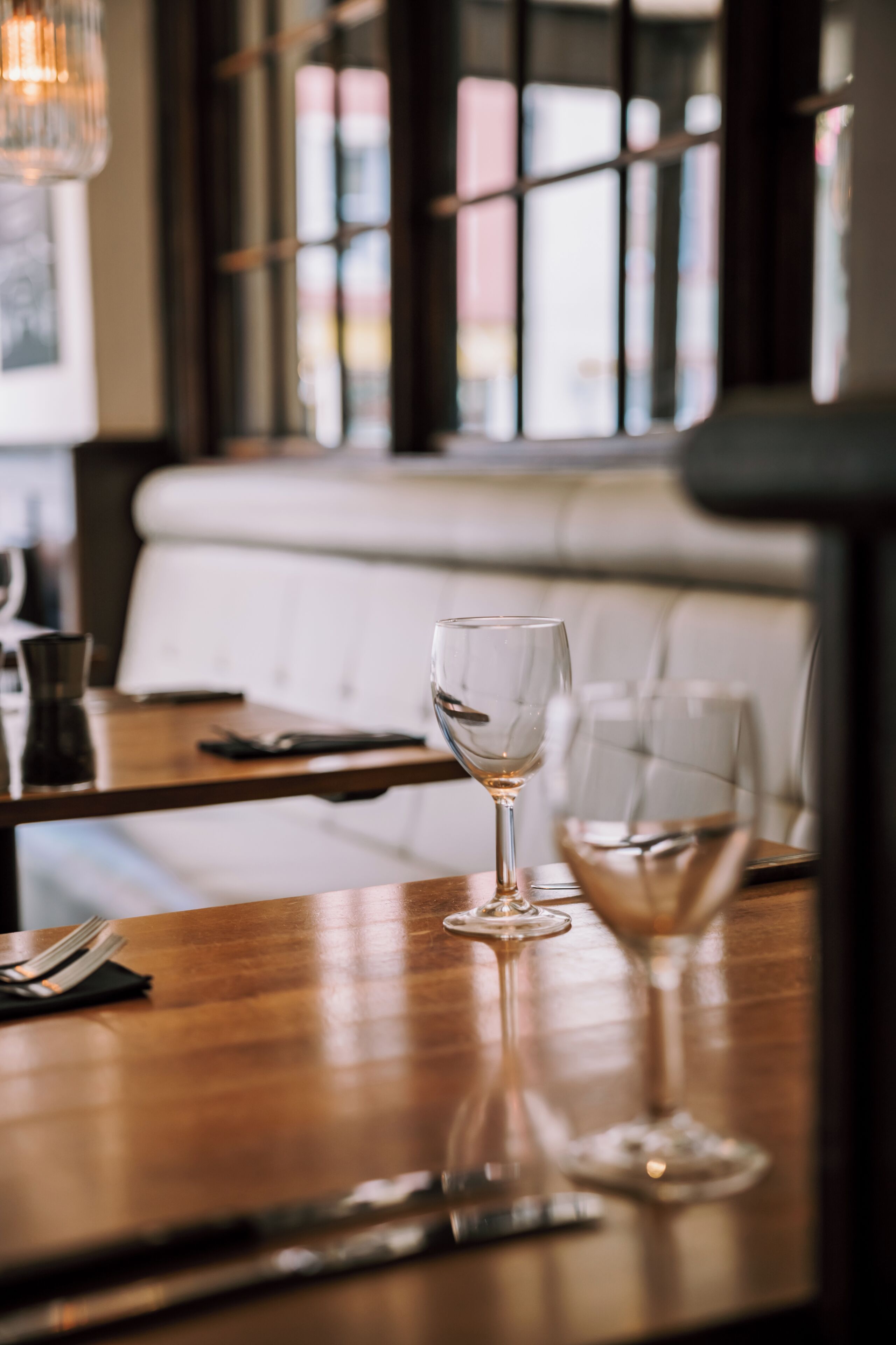A restaurant interior with a wooden table, two wine glasses, and a white cushioned bench.
