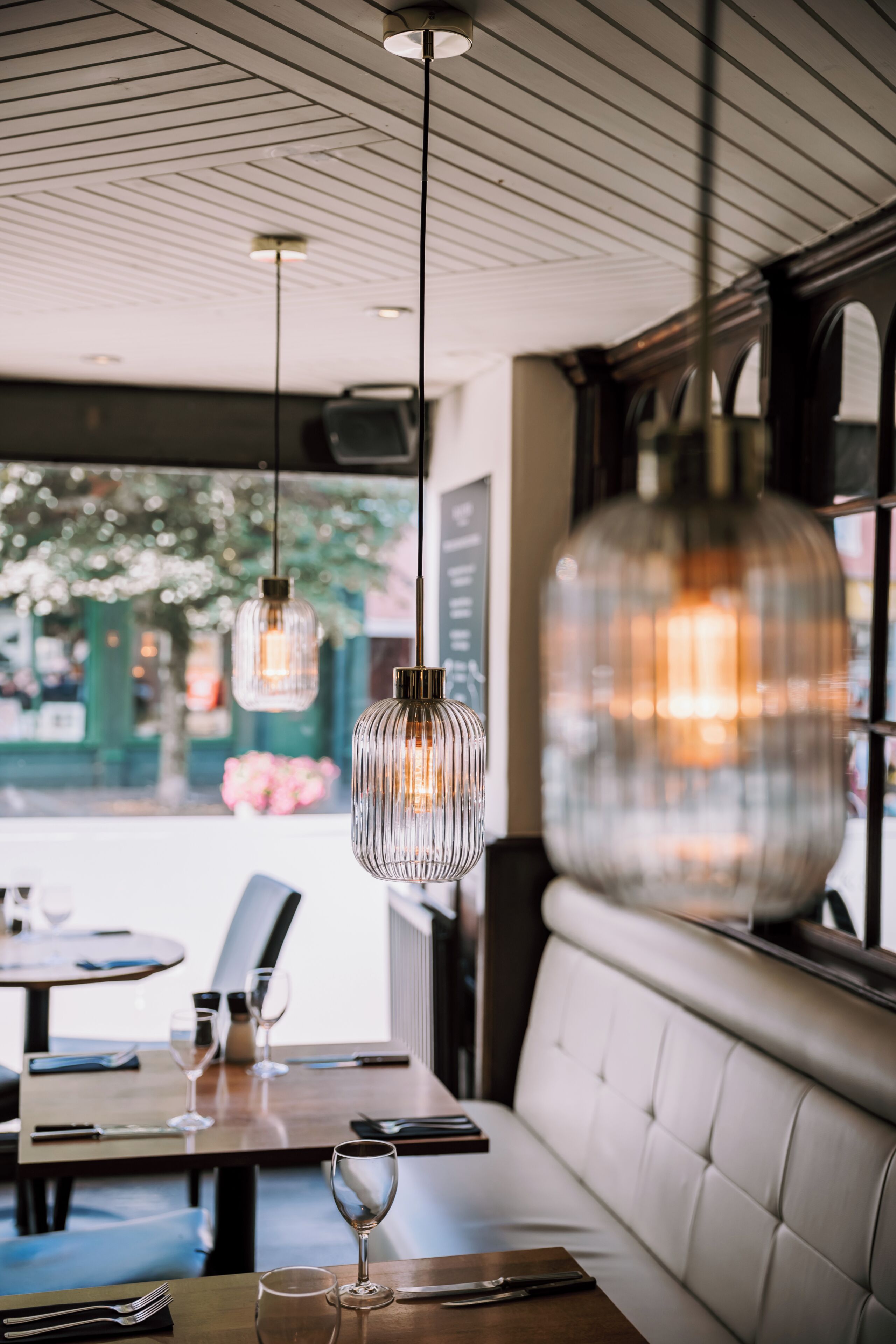 Een restaurantinterieur met hangende吊灯, een houten tafel en een beklede bank.