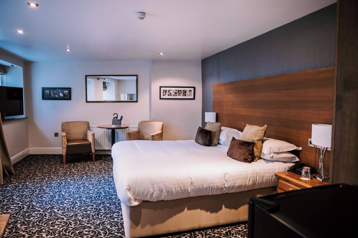 Una habitación de hotel con una cama grande, una silla, una mesita y un espejo en la pared.