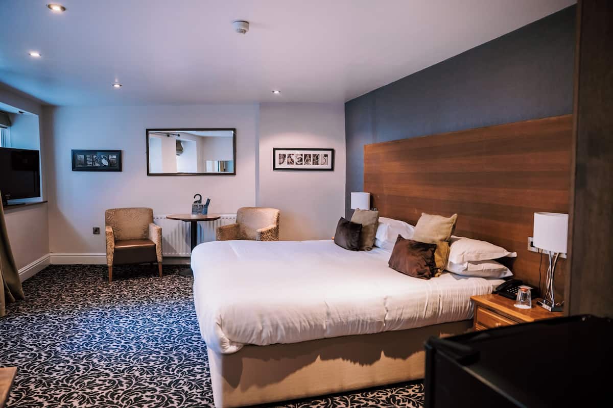 A hotel room with a large bed, a chair, a small table, and a mirror on the wall.