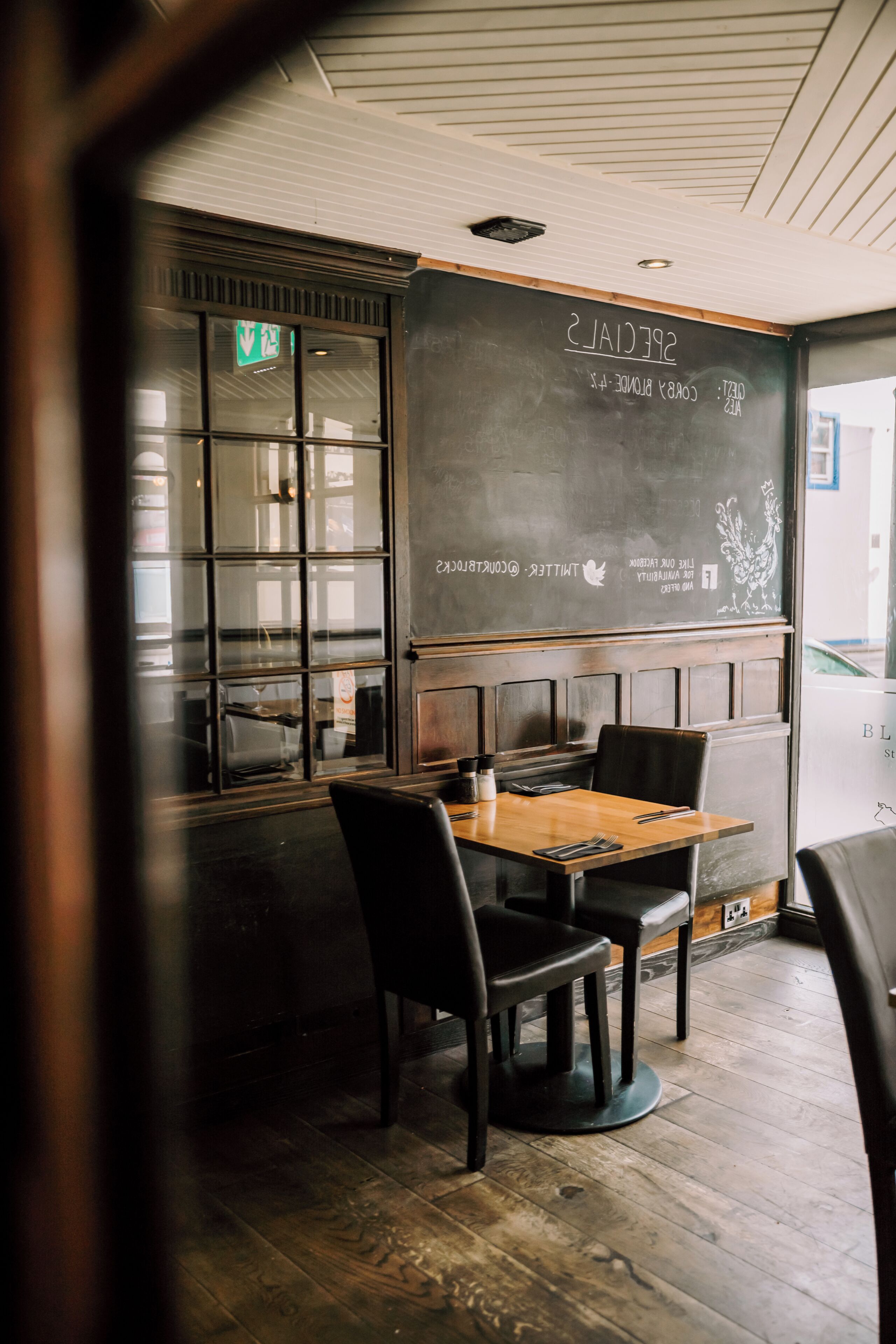 A restaurant interior with a chalkboard menu, wooden tables, and black chairs.