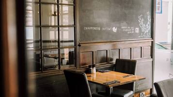 A restaurant interior with a chalkboard menu, wooden tables, and black chairs.