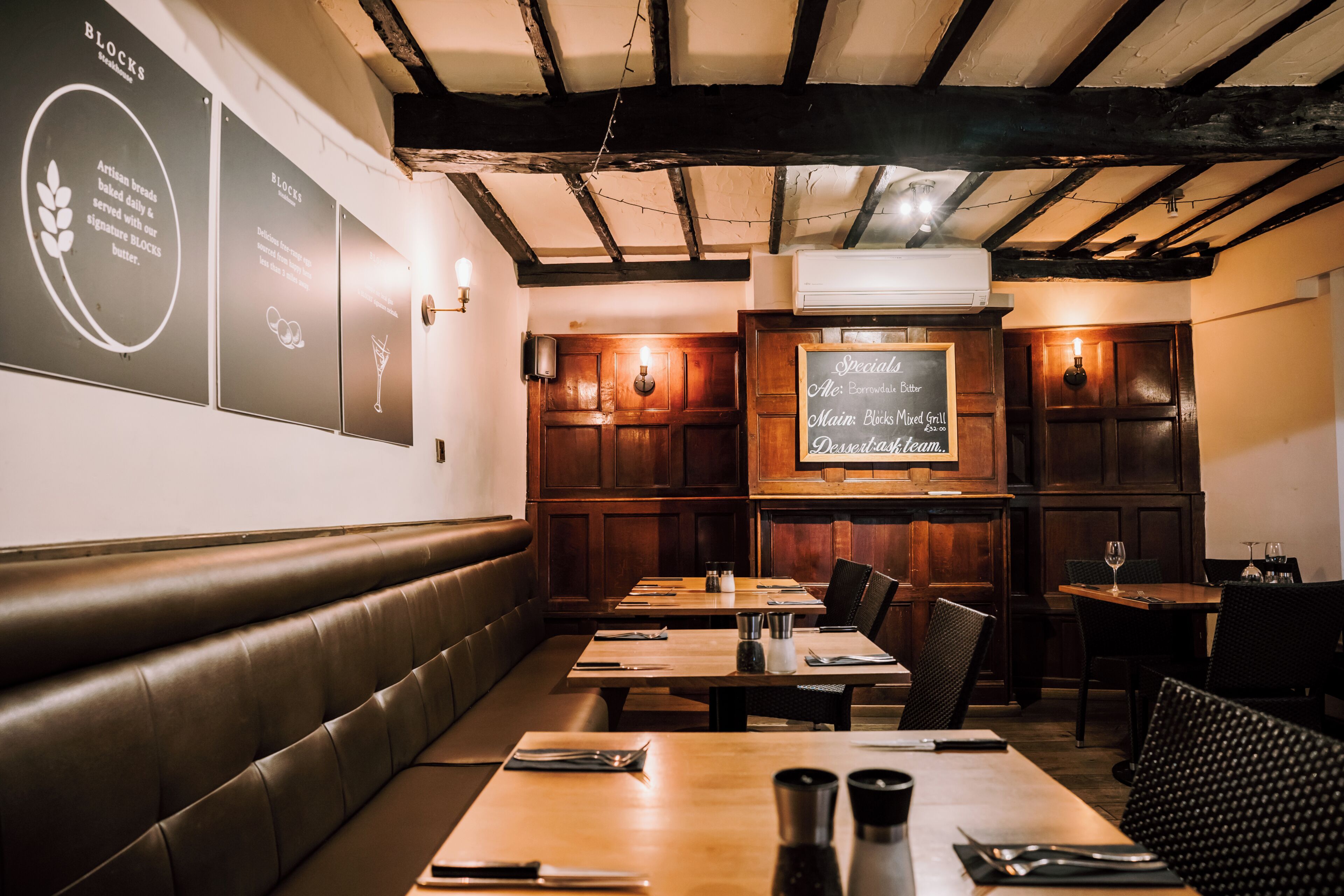 A restaurant interior with wooden tables, booths, and a menu board.