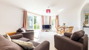 Ein modernes Wohnzimmer mit einer Sofagarnitur, einem Flachbildfernseher und einem Essbereich mit Tisch und Stühlen.