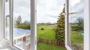 Blick aus einem Fenster auf ein Haus mit Rasen, einem Holzzaun und einem großen Baum.