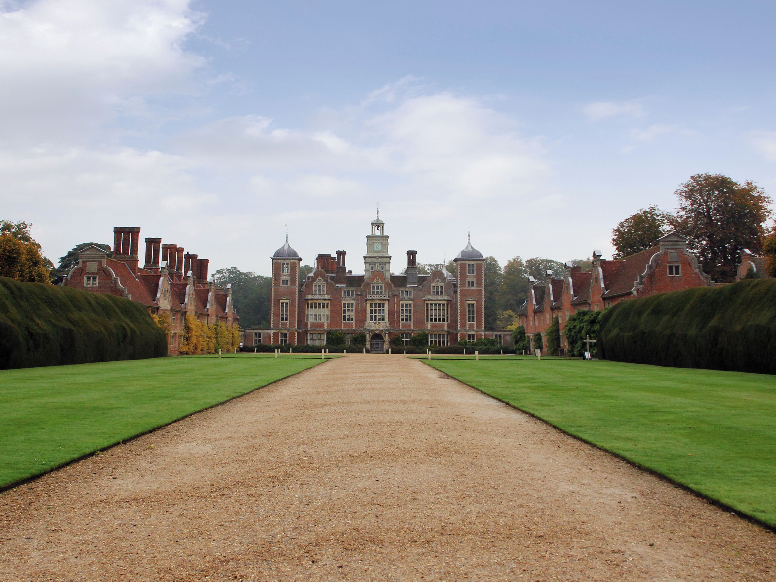 A large, historic building with a symmetrical facade, a central tower, and a gravel pathway leading to the entrance.