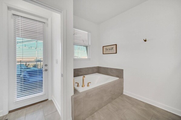 Un baño con una bañera blanca, baldosas color beige y una cita enmarcada en la pared.
