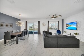 Ein modernes Wohnzimmer mit Essbereich, grauen Sofas, einem Fernseher und einem Deckenventilator.