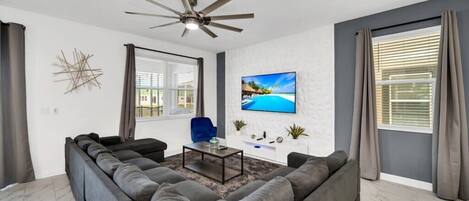 A modern living room with a sectional sofa, a coffee table, a ceiling fan, and a TV mounted on the wall.