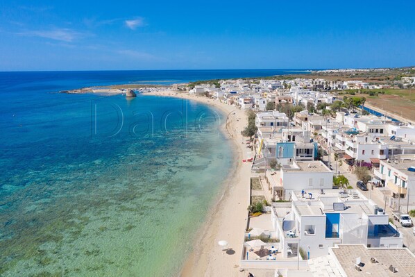 A coastal town with clear blue waters, a sandy beach, and white buildings with blue accents.