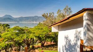Una casa con techo rojo, rodeada de exuberante vegetación y vistas a un lago y montañas.