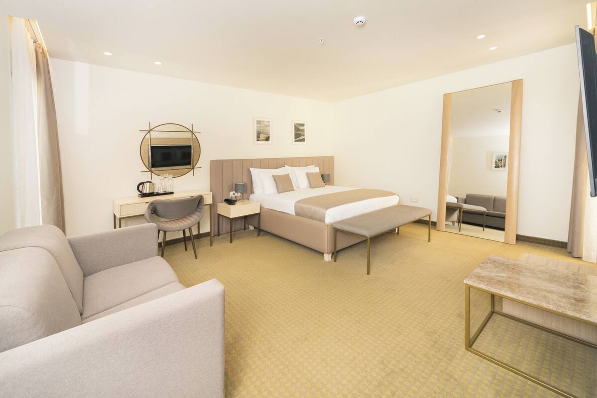A hotel room with a bed, a desk with a chair, a sofa, and a large mirror.