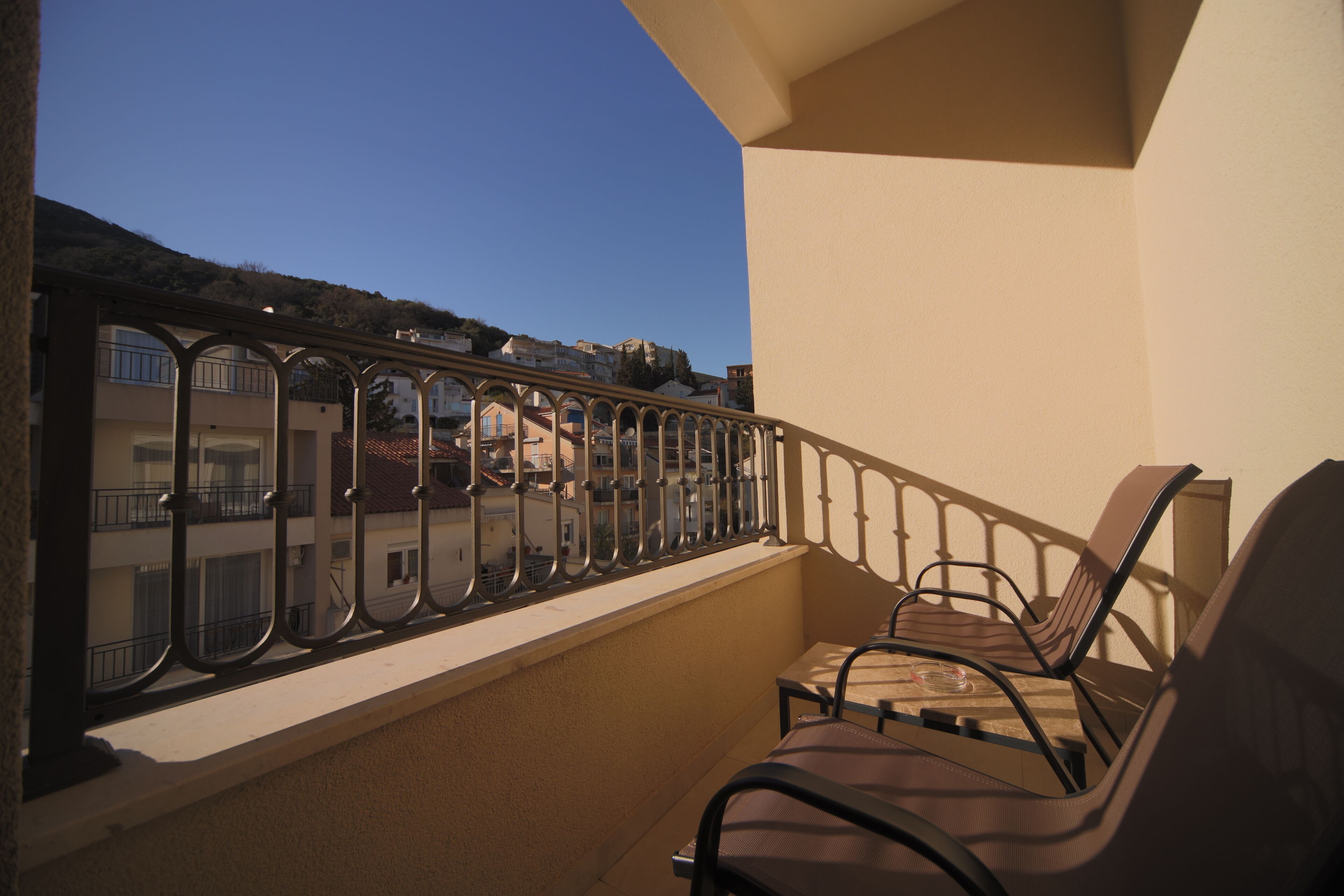 A balcony with a metal railing, two chairs, and a view of buildings in the background.