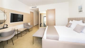 Ein modernes Hotelzimmer mit einem großen Bett, einem Schreibtisch mit Stuhl, einer Bank und einem an der Wand befestigten Fernseher.