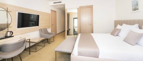A modern hotel room with a large bed, a desk with a chair, a bench, and a TV mounted on the wall.