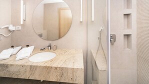 A modern bathroom with a marble sink, a large round mirror, and a glass-enclosed shower. - Hotel Pima Budva (Budva)