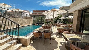 A poolside area with a clear pool, outdoor seating, and a staircase leading to an upper level. - Hotel Pima Budva (Budva)