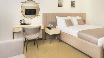 A hotel room with a bed, a desk, a chair, a bedside table, and a mirror.