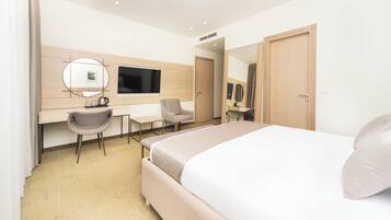 Una habitación de hotel moderna con una cama grande, un escritorio con computadora, una silla y un televisor.