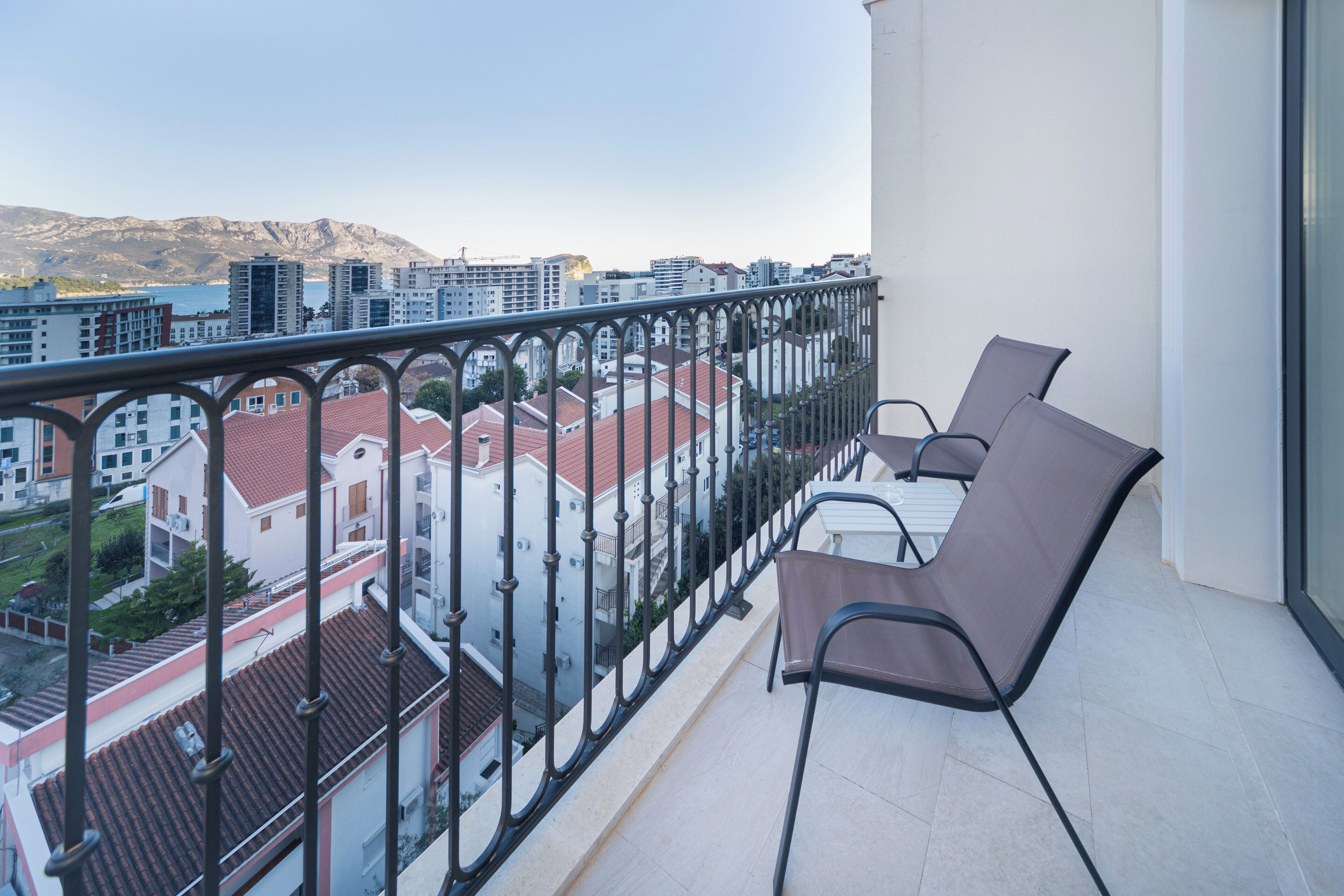 Een balkon met een metalen hekwerk, twee stoelen en een tafel.