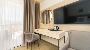 A hotel room with a desk, a chair, a sofa, a large TV, and a window with curtains. - Hotel Pima Budva (Budva)