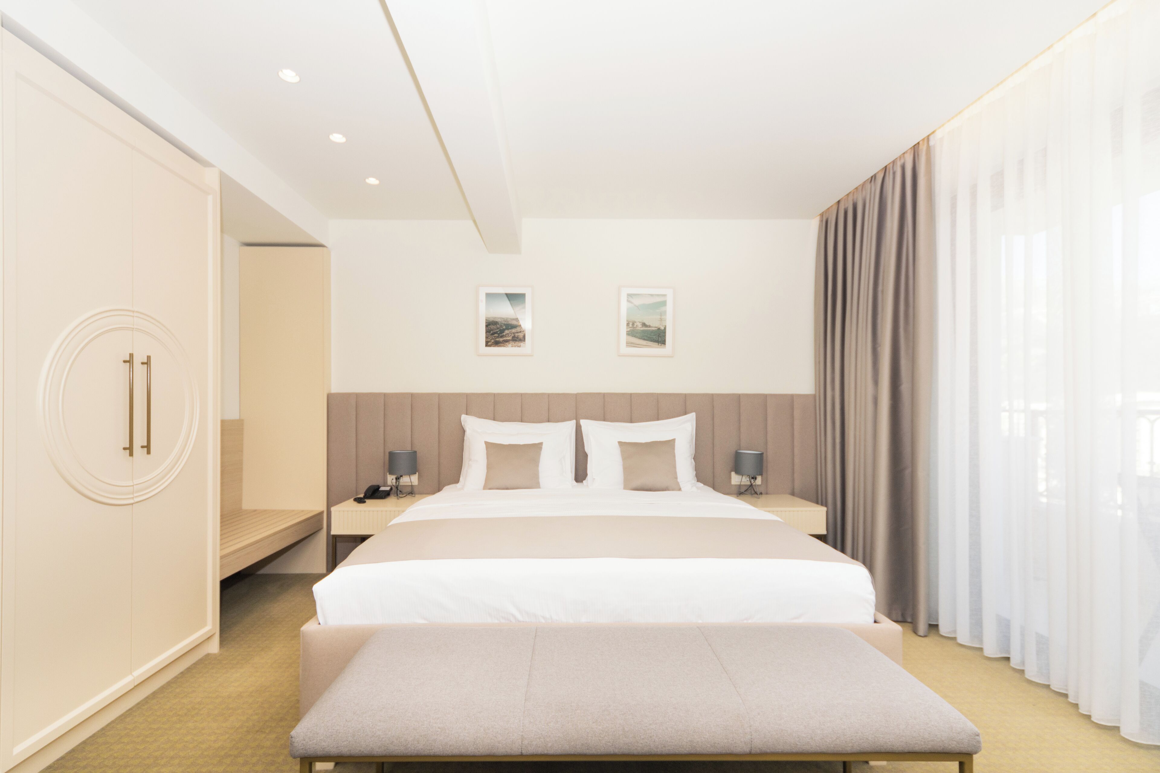 Una habitación de hotel moderna con una cama grande, mesitas de noche, un banco y un armario.