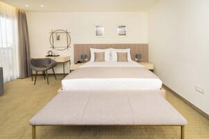 A hotel room with a large bed, a desk, a chair, and two bedside tables with lamps.
