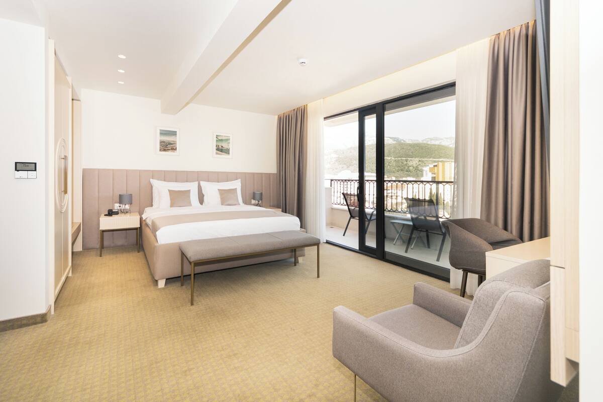 A hotel room with a bed, bedside table, lamp, and a view of the balcony.