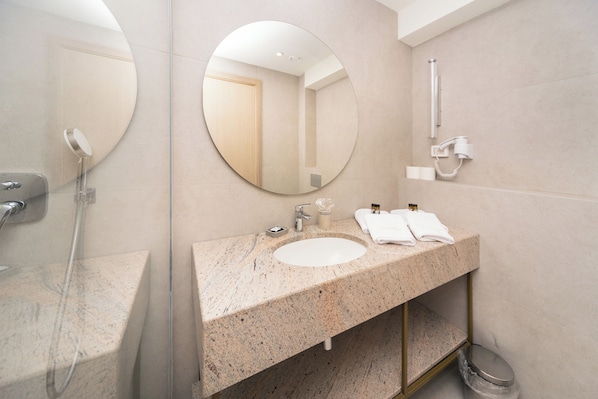 Un baño moderno con encimera de granito, un espejo redondo, un cabezal de ducha de mano y un perchero.