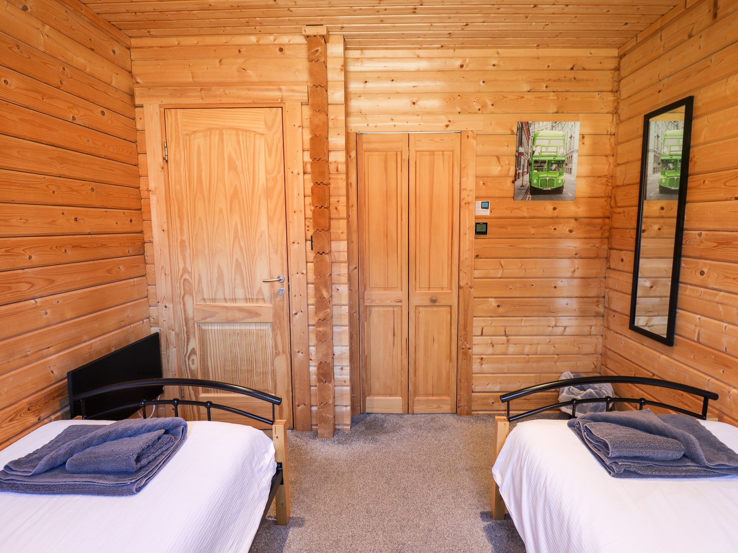 Habitación de cabaña de madera con dos camas, un espejo y una puerta.