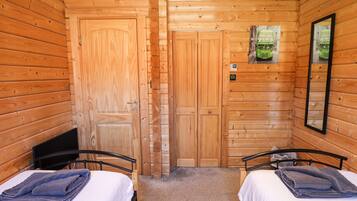 Habitación de cabaña de madera con dos camas, un espejo y una puerta.