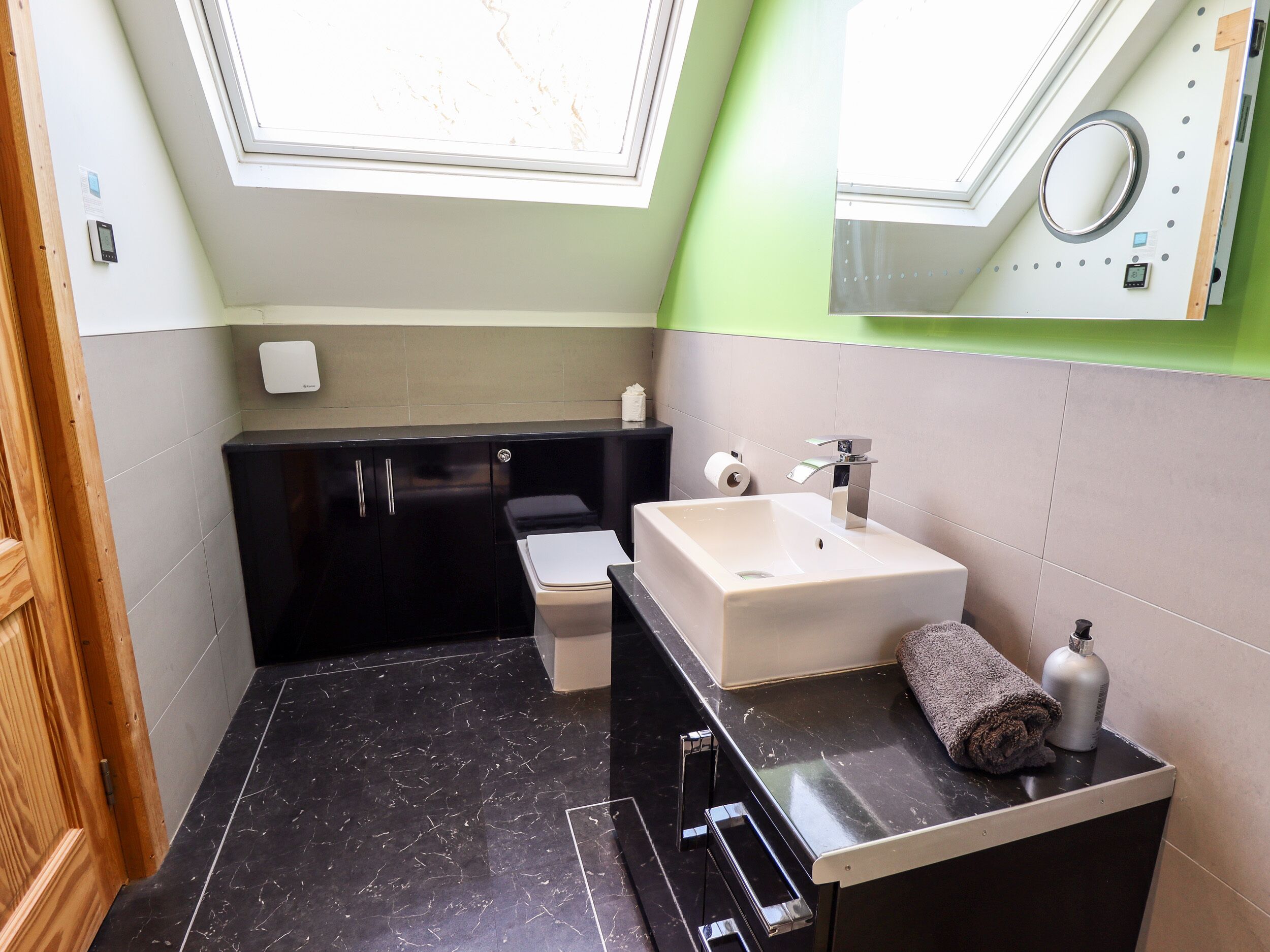 A modern bathroom with a black vanity, a white sink, and a green accent wall.