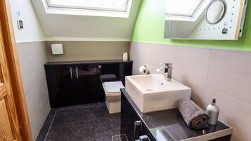 A modern bathroom with a black vanity, a white sink, and a green accent wall.