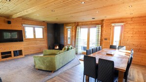 A cozy cabin interior with a fireplace, a sofa, a dining table with chairs, and a TV mounted on the wall. - Ilodge Ultra (Louth)