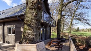 A wooden cabin with a deck, a large tree, and a picnic table. - Ilodge Ultra (Louth)