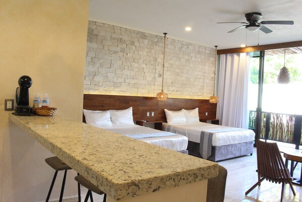 A hotel room with a kitchen area, two beds, a dining table, and a balcony with a view.