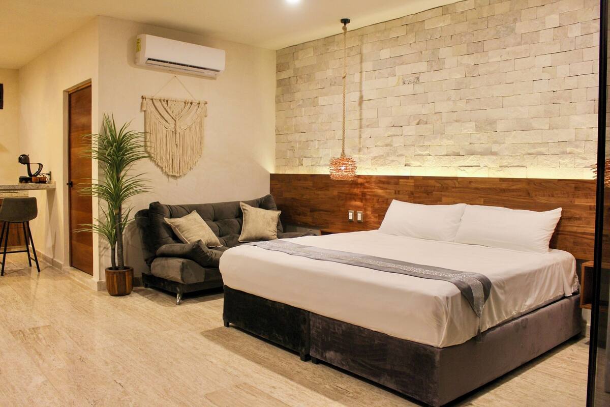 Un dormitorio con una cama grande, cabecera de madera, pared de piedra, lámpara colgante y una planta en maceta.