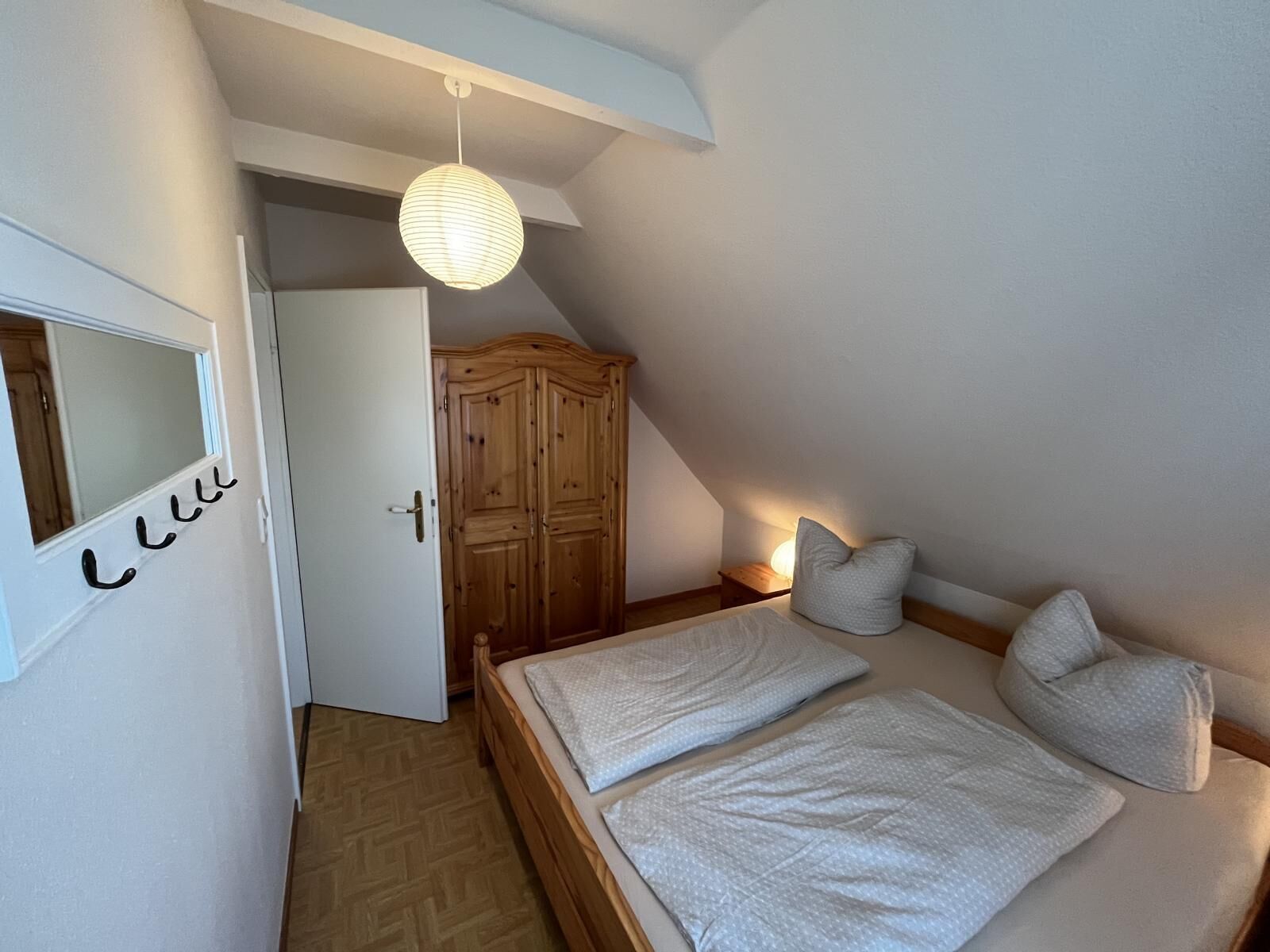 A bedroom with a bed, a wardrobe, a mirror, and a hanging light fixture.