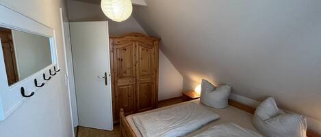 A bedroom with a bed, a wardrobe, a mirror, and a hanging light fixture.