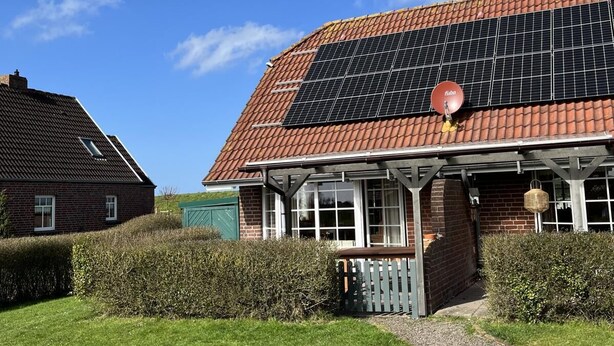 A house with a solar panel roof, a brick exterior, and a well-maintained lawn. - Vacation home Deichblick (Neßmersiel)