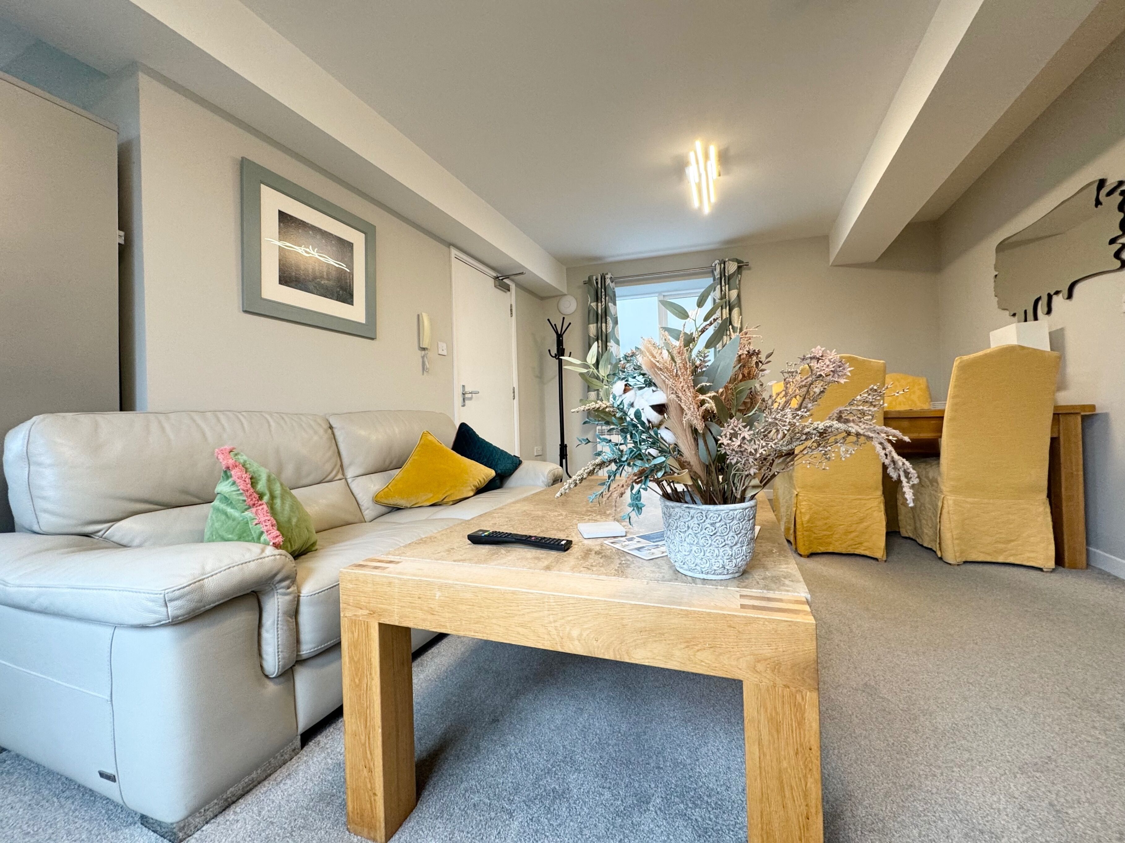 A modern living room with a beige leather sofa, a wooden coffee table, and a vase with dried flowers.
