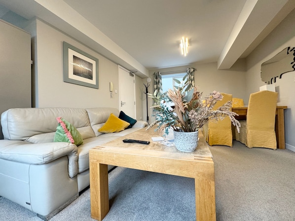 A modern living room with a beige leather sofa, a wooden coffee table, and a vase with dried flowers.