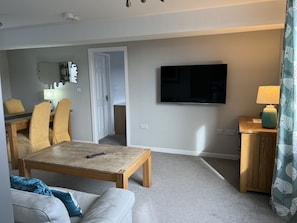 A living room with a TV, a dining area with chairs, a sofa, and a small table.