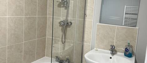 A bathroom with a glass-enclosed shower, a white sink, and a mirror above it.
