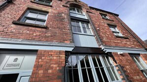 A brick building with multiple windows and a sign indicating 'Warehouse Apartments'. - The Market Street Apartments - Ulverston (Ulverston)