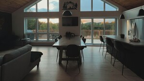 A spacious kitchen with a large dining table, high ceilings, and large windows offering views of a deck and mountains. - The Double Diamant (St-Côme)