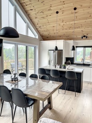 A modern kitchen with a large island, pendant lights, and a view of the outdoors. - The Double Diamant (St-Côme)