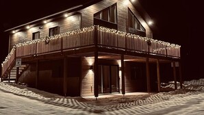 A two-story wooden building with a balcony, large windows, and a snow-covered ground. - The Double Diamant (St-Côme)